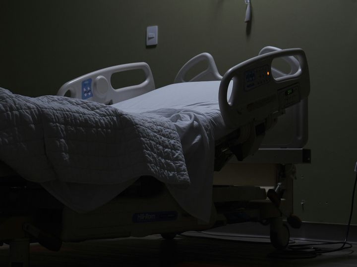 An empty hospital bed sits in a dimly lit room.