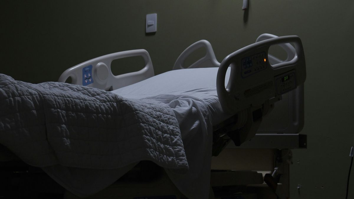 An empty hospital bed sits in a dimly lit room.
